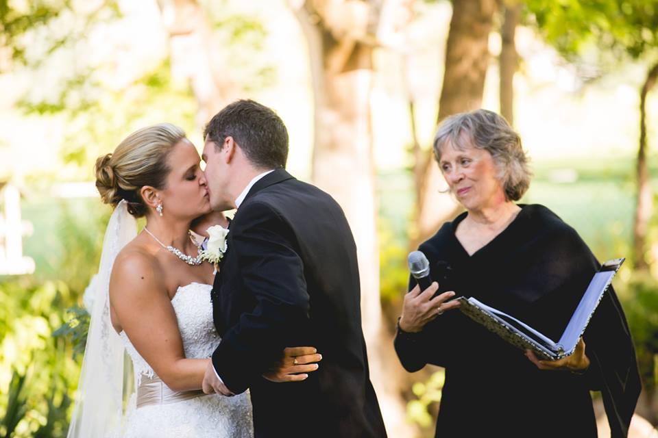 A bride and groom kissing in front of an older woman.