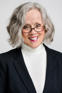 A woman with grey hair wearing glasses and a black jacket.
